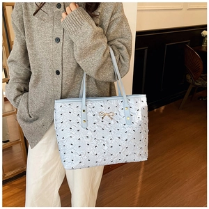 Détail du sac cabas matelassé bleu clair avec nœuds noirs et boucle dorée porté par un mannequin