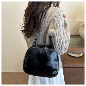 Minimalist black glossy shoulder bag shown on model in a warm home setting