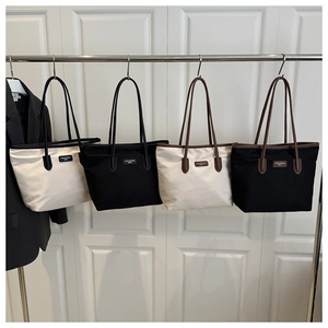 Detailed row of large nylon tote bags in beige and black with leather shoulder straps