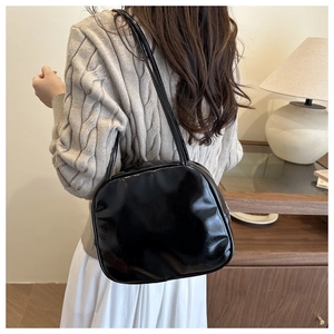 Chic black glossy shoulder bag with dual slim straps worn in a modern home setting