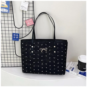 Détail du sac cabas matelassé noir avec motifs nœuds blancs et décoration dorée