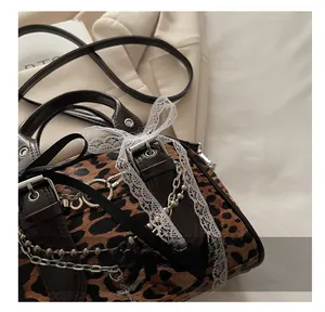Detailed close-up of leopard print handbag with metallic chains and white lace bow