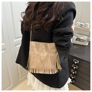 Sac bandoulière beige en cuir PU avec pompons porté par un mannequin en décor décontracté