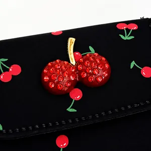 Détail d'un charm cerise en strass rouges sur un sac à bandoulière imprimé