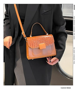 Detail of brown faux leather crossbody bag with crocodile embossed flap on black blazer