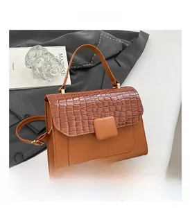 Detail of a brown croc-textured crossbody bag with fixed handle and adjustable strap