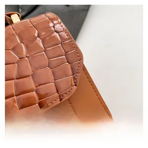 Close-up of brown crocodile embossed leather bag with shiny gold square metal buckle
