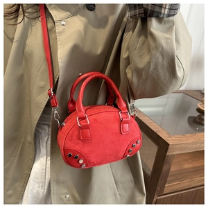 Close-up of a red suede crescent bag with silver rivet details on a beige trench coat