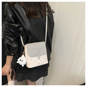 Detail of crossbody bag with heart-shaped metal buckle and a white plush pompom charm