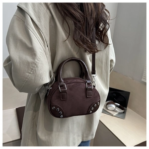 Detail of dark brown suede bow bag with silver studs worn by a model in a minimal interior