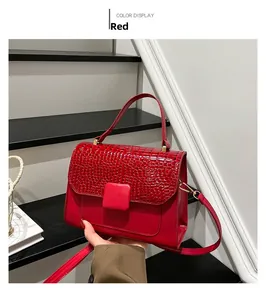 Detail of red crossbody bag with crocodile embossed flap and square metallic buckle