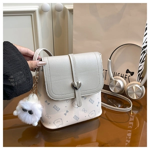 Detail of cream crossbody bag with cat pattern, heart buckle and white furry pendant