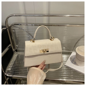 Detail of a creamy white crossbody bag with gold metal turn-lock on a modern shelf