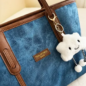 Close-up of denim tote bag with leather trim and cute white cloud plush pendant charm
