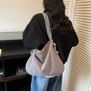 Grand sac hobo en velours côtelé gris foncé avec bandoulière tissée porté par un mannequin