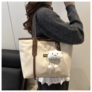 Close-up of beige tote bag with brown leather handles and plush cloud charm accessory