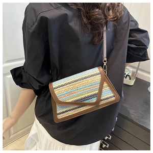 Detailed close-up of a colorful woven straw envelope crossbody bag with leather trim