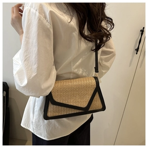 Detail of woven straw envelope crossbody bag with black trim worn by a model