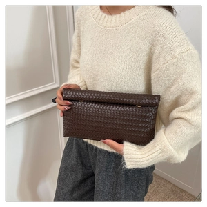 Close-up of deep brown woven leather clutch bag with premium matte texture and metal clasp