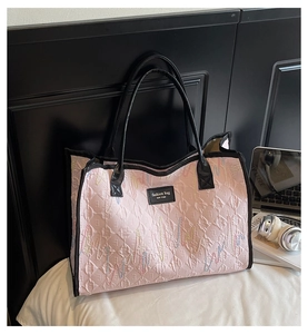 Detail of pink quilted tote bag with colorful embroidery and black leather handles