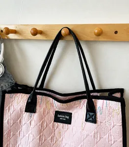 Pink quilted tote bag hanging on a hook featuring black leather straps and fashion label