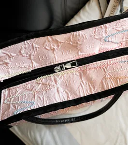 Close-up of pink embossed fabric tote bag featuring silver zipper and black strap details