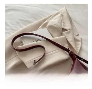 Dettaglio borsa hobo bordeaux in ecopelle con fibbie su un blazer bianco e libro