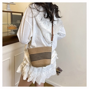 Détail du sac seau en paille tressé à rayures noires et bandoulière en cuir brun