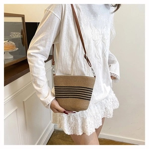 Détail du sac seau en paille tissée avec rayures noires et bandoulière en cuir marron