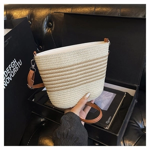 Détail du sac seau tissé à rayures avec texture beige et bandoulière en cuir sur boîte cadeau