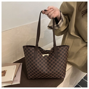 Brown tote bag with M-letter pattern and gold metal clasp in an elegant street setting
