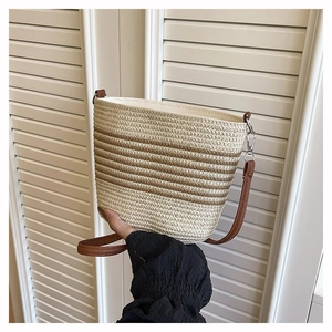 Détail du sac seau tissé avec bandoulière en cuir marron et rayures en paille beige