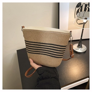 Détail du sac seau en paille tissée avec rayures noires et bandoulière en cuir marron