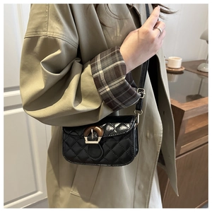 Detail of black quilted shoulder bag featuring a unique wood grain buckle and slim strap