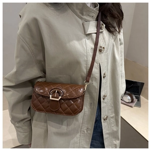 Close-up of brown quilted crossbody bag with horseshoe buckle worn by a model in a cafe