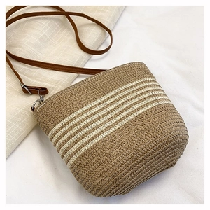 Détail d'un sac seau en paille tissée à rayures avec fermeture éclair sur tissu blanc texturé