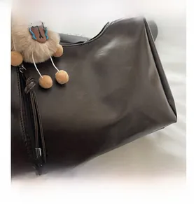 Detailansicht der braunen Ledertasche mit Silberlogo und khakifarbenem Plüsch-Anhänger