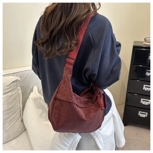 Detail of burgundy tote bag with wide shoulder strap and woven zipper pull decoration