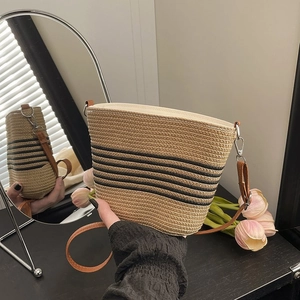 Détail du sac seau en paille tissée avec rayures noires et bandoulière en cuir marron