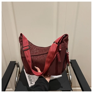 Detail of dark red leopard print crescent bag with wide strap and woven cord accents