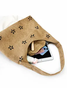 Detail view of large brown suede tote with laser-cut floral patterns and inner pouch