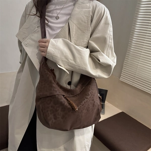Brown leopard print crescent tote bag with a wide strap on a model wearing a trench coat
