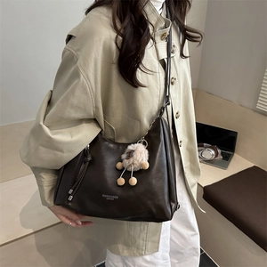 Vintage dunkelbraune Halbmond-Schultertasche mit Bärenanhänger am beigen Trenchcoat
