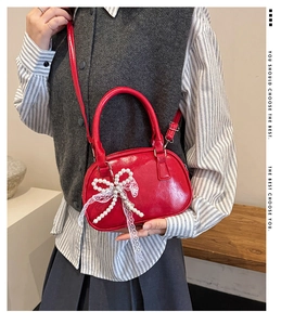 Detail of red glossy patent leather bag with pearl bow accessory shown on shoulder