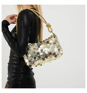 Detail of gold sequin shoulder bag with knotted strap worn against a black dress