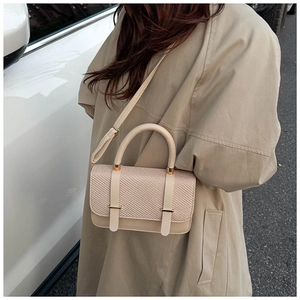 Détail d'un sac à main beige avec rabat tissé et boucles dorées porté sur un trench-coat