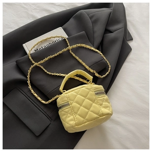 Détail d'un sac vanity jaune vif matelassé avec chaîne dorée posé sur un blazer noir