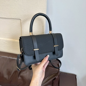 Sac à bandoulière noir avec rabat tissé et détails dorés tenu par la poignée