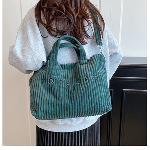 Détail d'un grand sac cabas en velours côtelé vert foncé porté par un mannequin