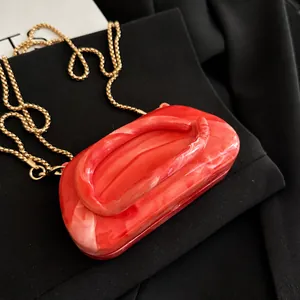 Detailed close-up of red marble pattern acrylic clutch bag with golden chain strap